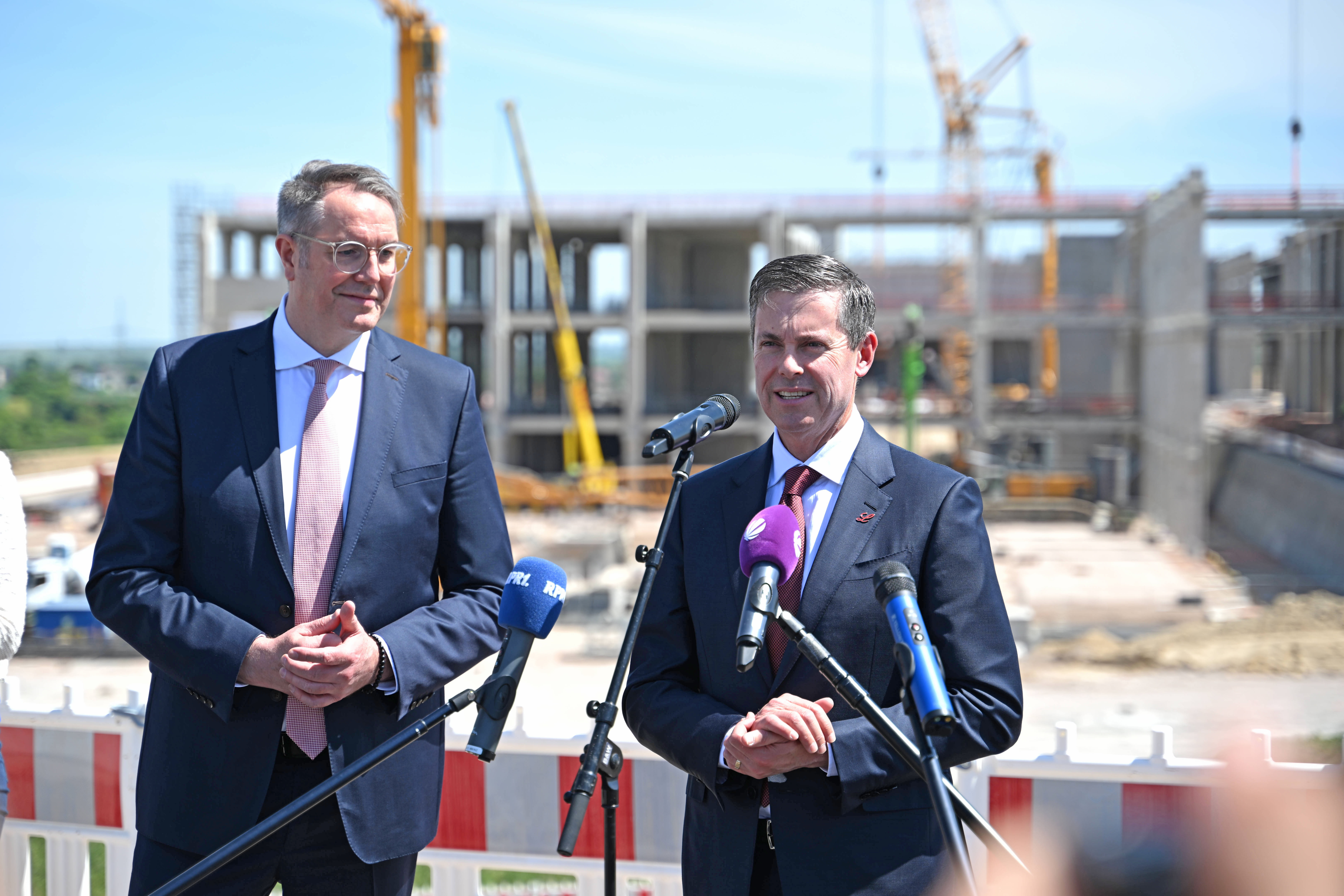 Dave Ricks spricht ins Mikrofon; links von ihm steht Minister Alexander Schweitzer.

