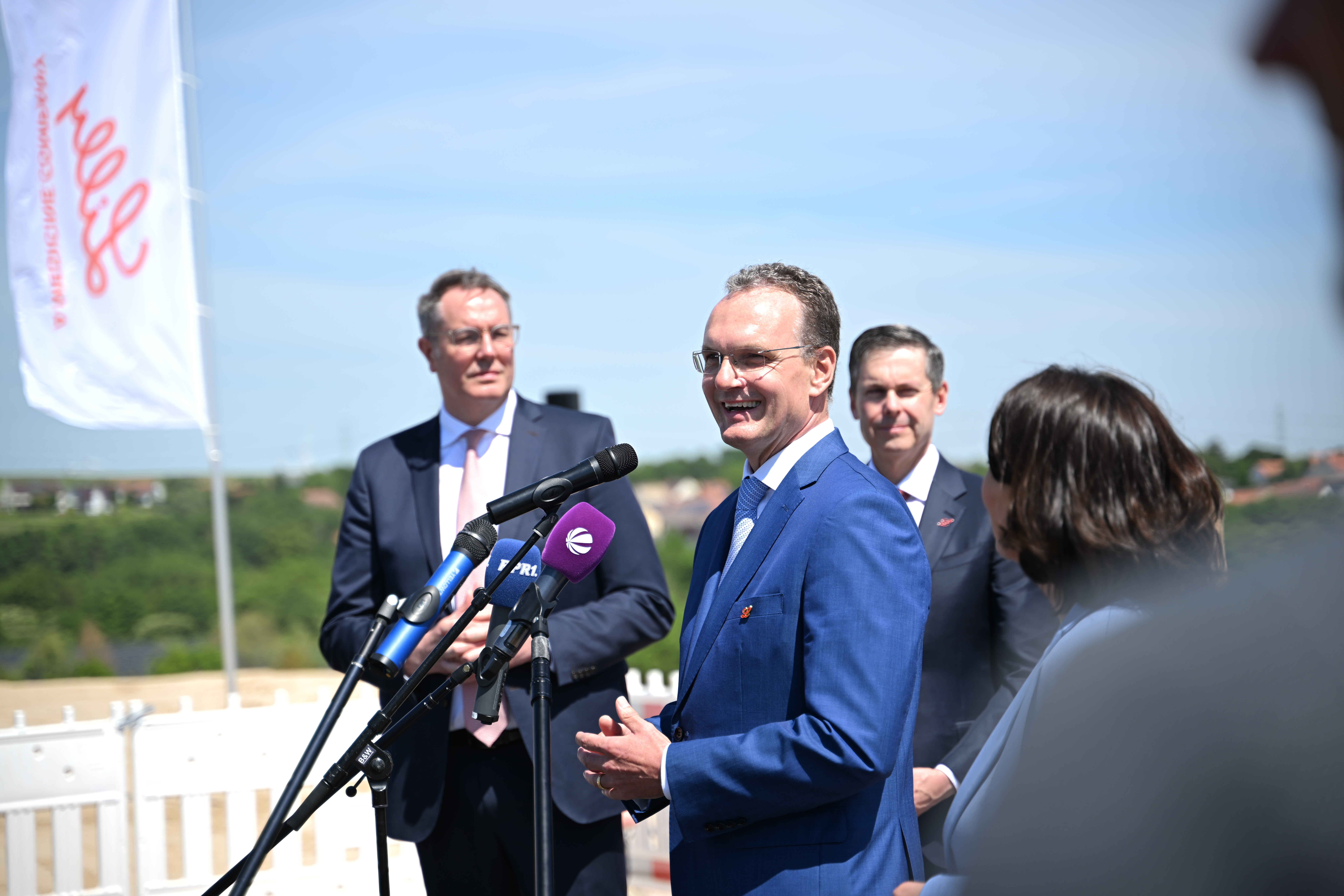 Alexander Horn spricht ins Mikrofon; im Hintergrund Dave Ricks und Minister Alexander Schweitzer
