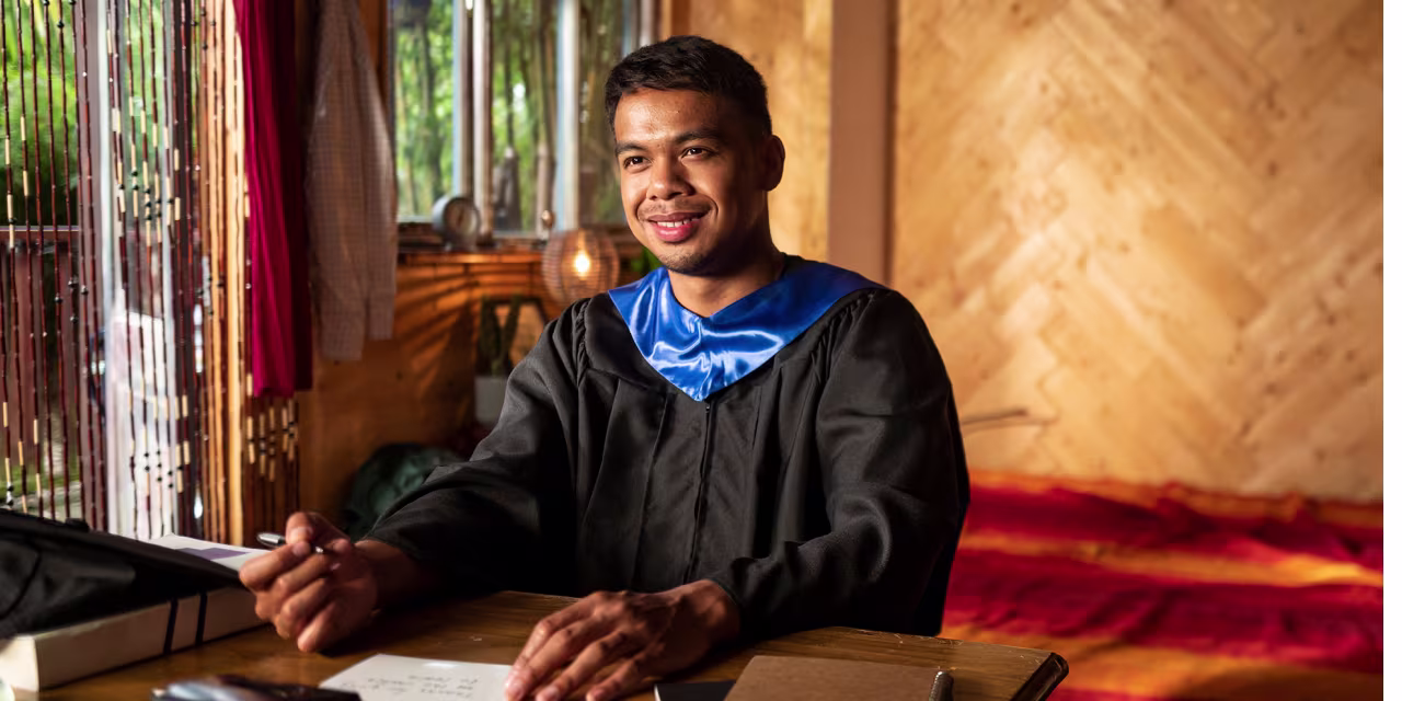 howsendSML An image of a man smiling, wearing a graduation robe