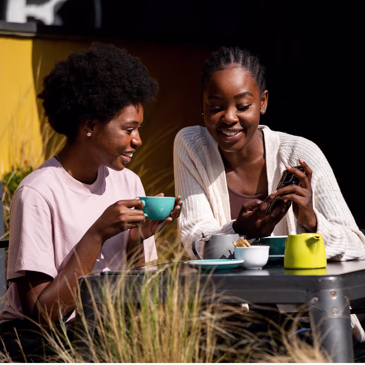 Two African women sitting outside at a Coffee shop and smiling