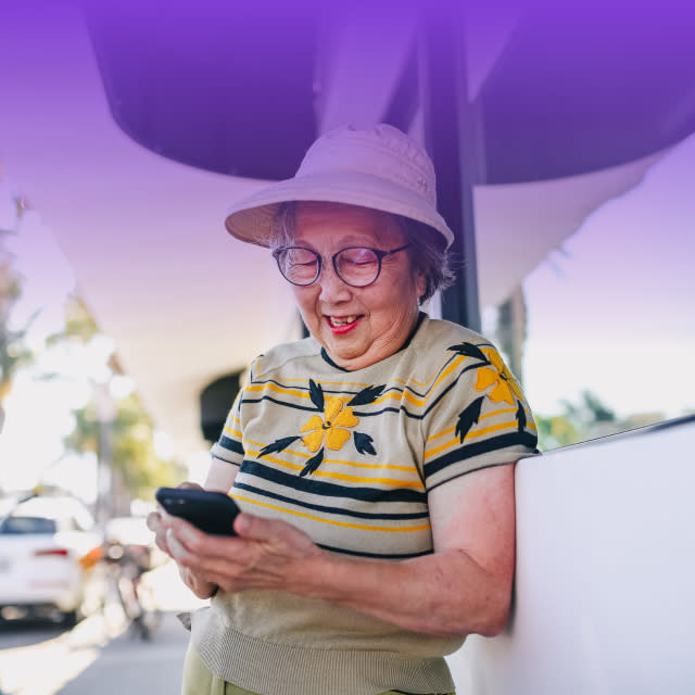 An image of an older lady wearing a hat and glasses, using her phone