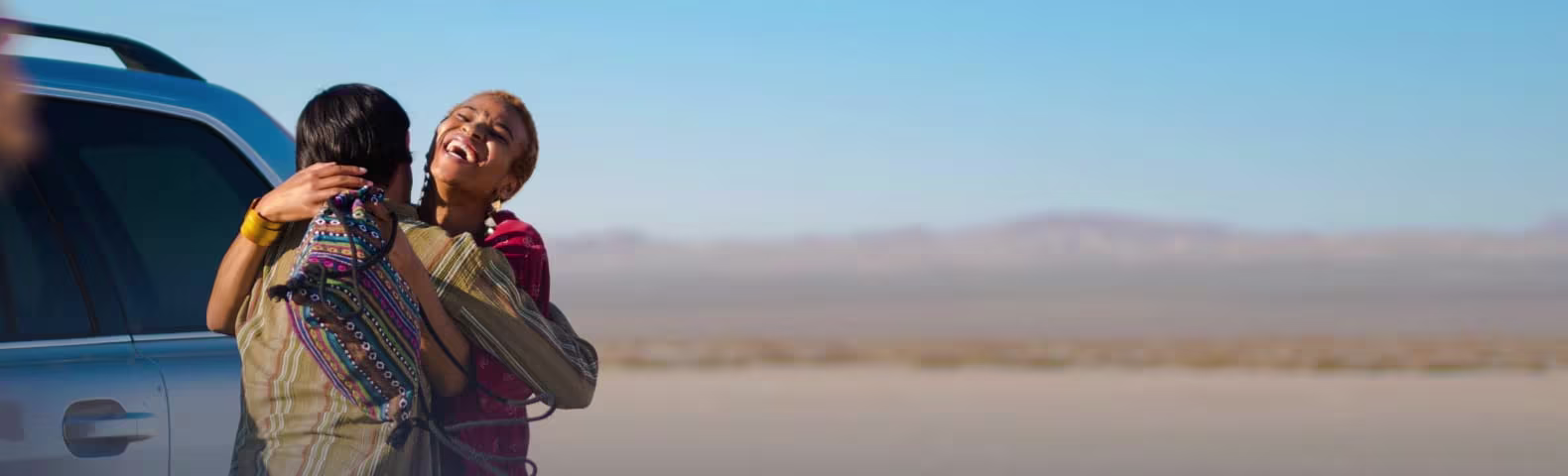 Joven pareja africana se abraza en la parte trasera de una camioneta con un desierto de fondo.