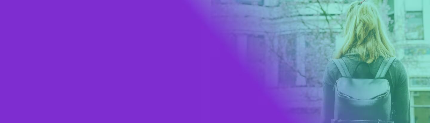 The back of a female student who is wearing a backpack and looking at a campus building