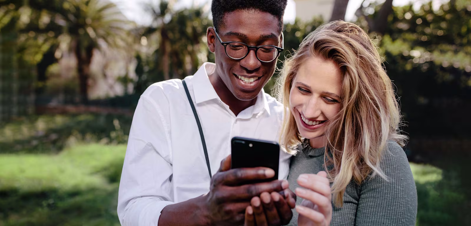 How exchange rates work A man wearing glasses, showing his phone screen to a blonde girl stood next to him