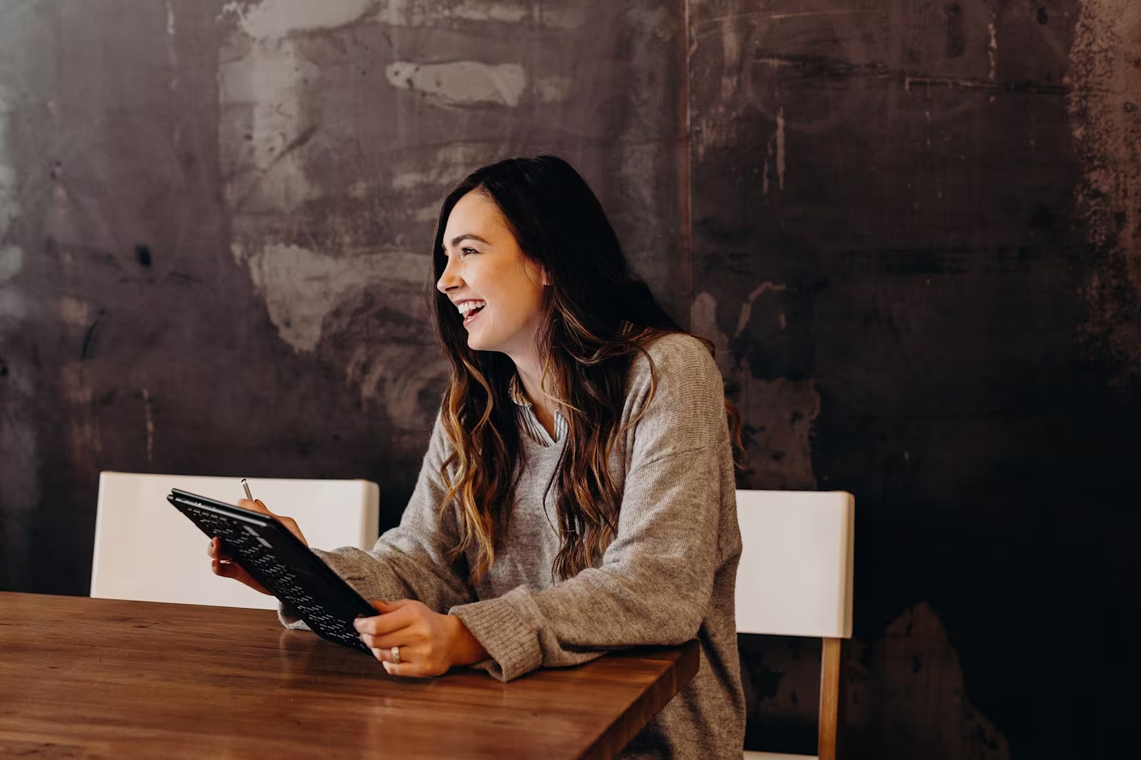 A woman looking away from the camera and smiling whilst holding a tablet and stylus pen in her hands