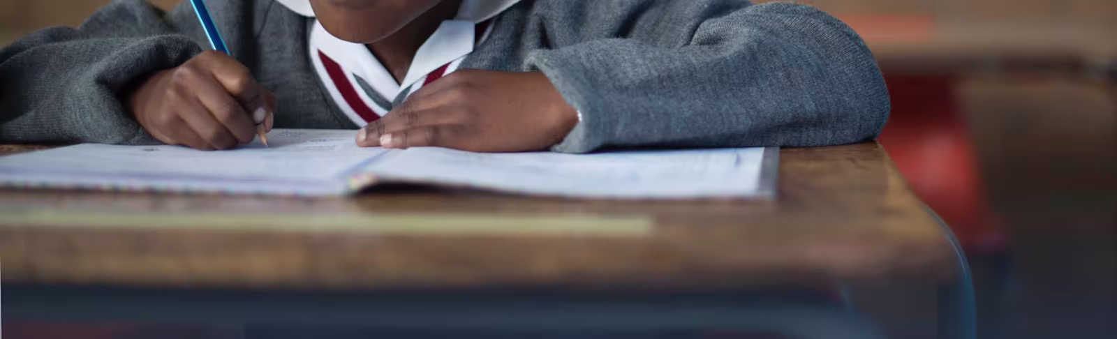 africa Close up of small child in school uniform writing in exercise book.