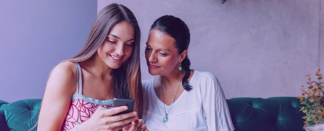 Two women sat next to each other, looking at a smartphone and smiling