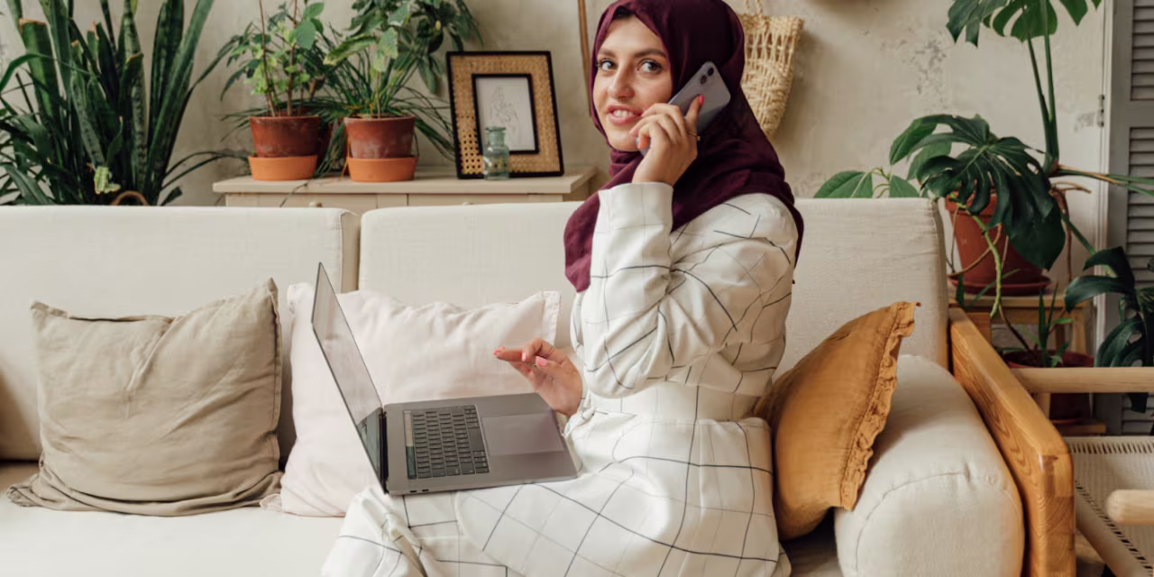 An image of a lady sat on her phone and using her laptop, whilst sat on the sofa