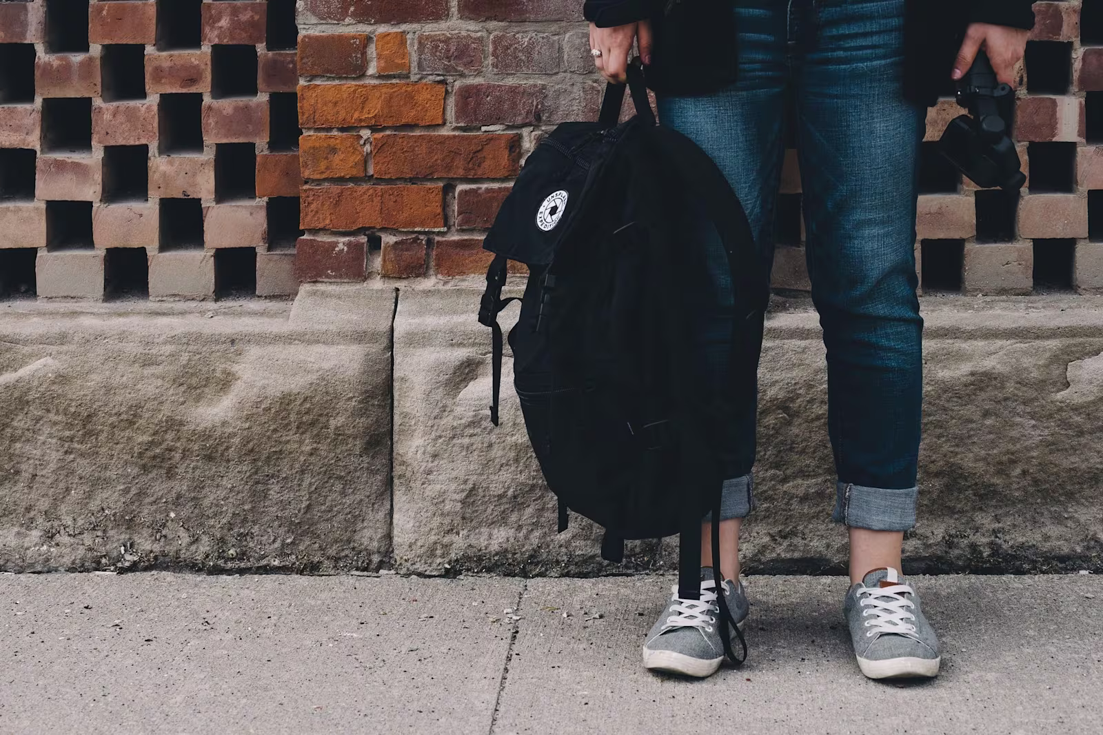 Niño sujetando su mochila del colegio Niño sujetando la mochila del colegio con su mano izquierda. En la imagen únicamente se ven los pies del niño.