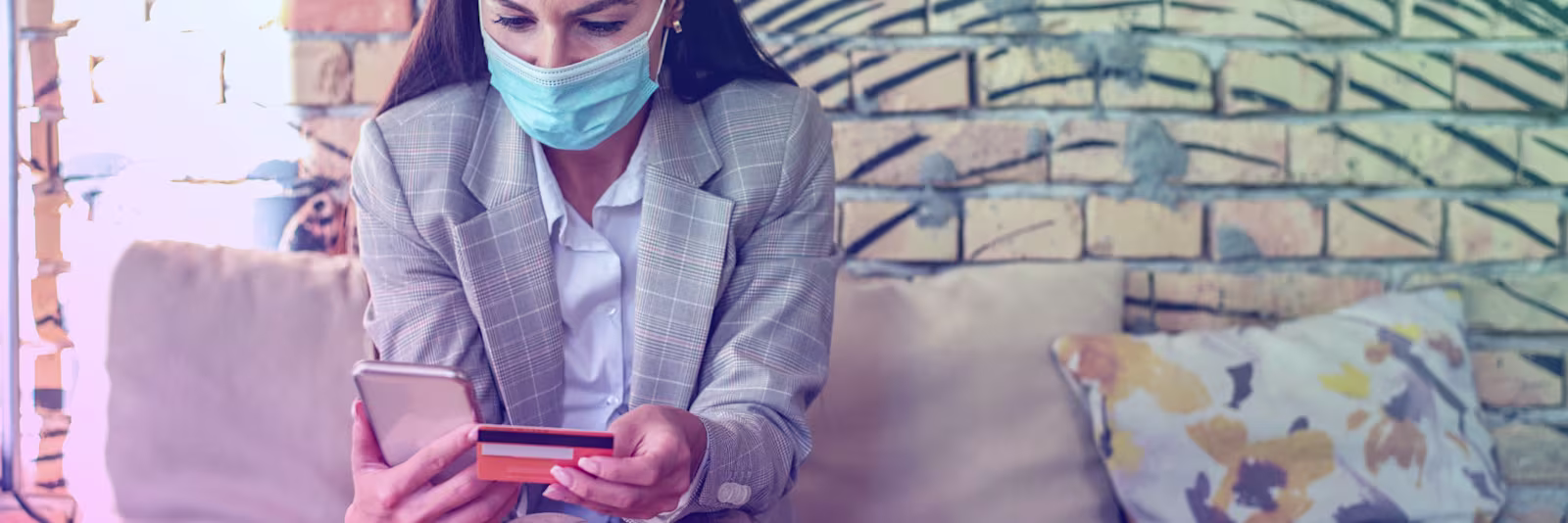 header-covid19-scams An image of someone wearing a mask whilst using their phone