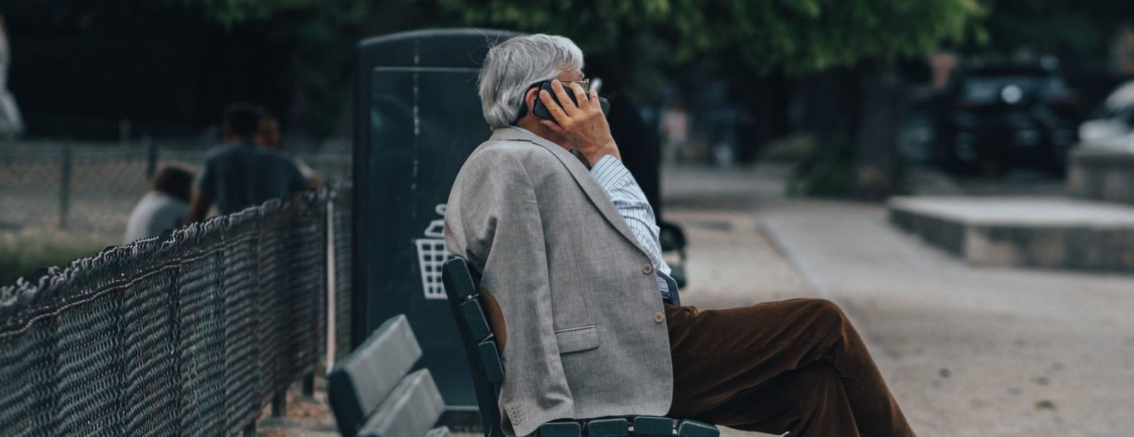 A photo of a man sitting on a bench outdoors whilst on a phone call