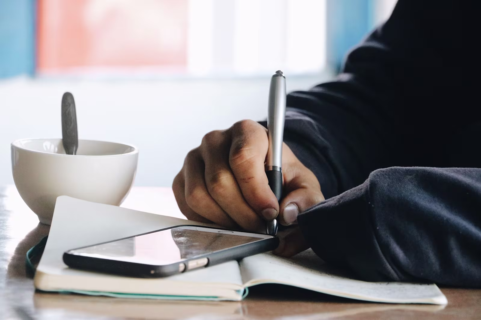 A close up image of a man writing on a notebook at a coffee shop