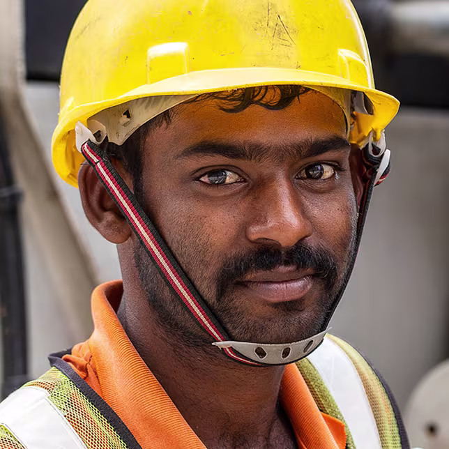 A photo of a migrant construction worker wearing a yellow helmet and hi-vis jacket