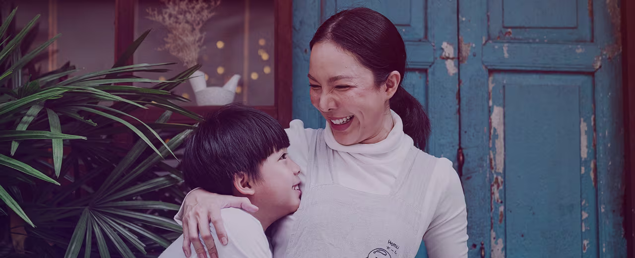 Philippines Desktop Hero Image An image of a lady laughing, with her arms around a young boy to her left.