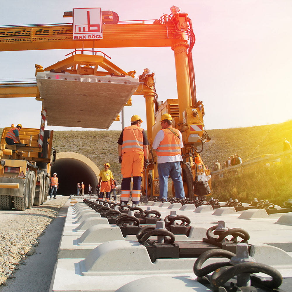 Das Bild zeigt Arbeiter in oranger Arbeitsuniform. Sie verlegen neue Gleise. Ein Kran im Hintergrund hebt schwere Betonteile hoch. 
Copyright: Deutsche Bahn AG/ Frank Kniestedt
