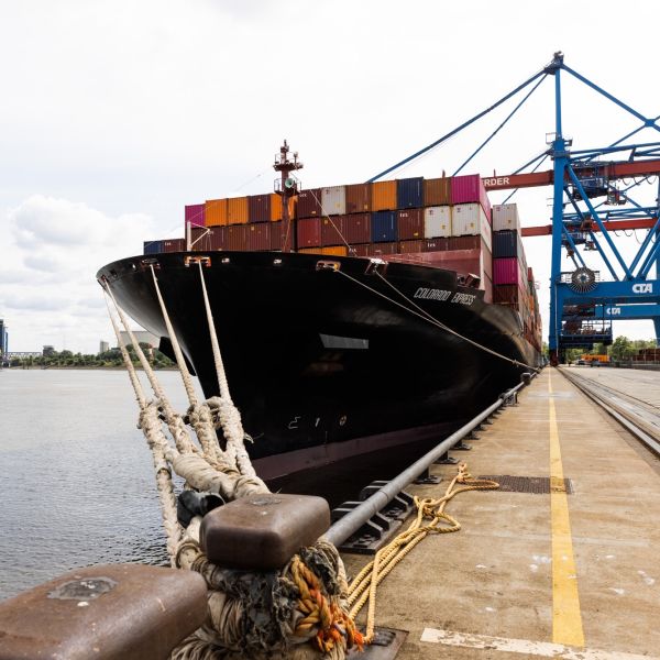 Man sieht ein Frachtschiff mit Containern beladen, dass in Containerterminal ankert.