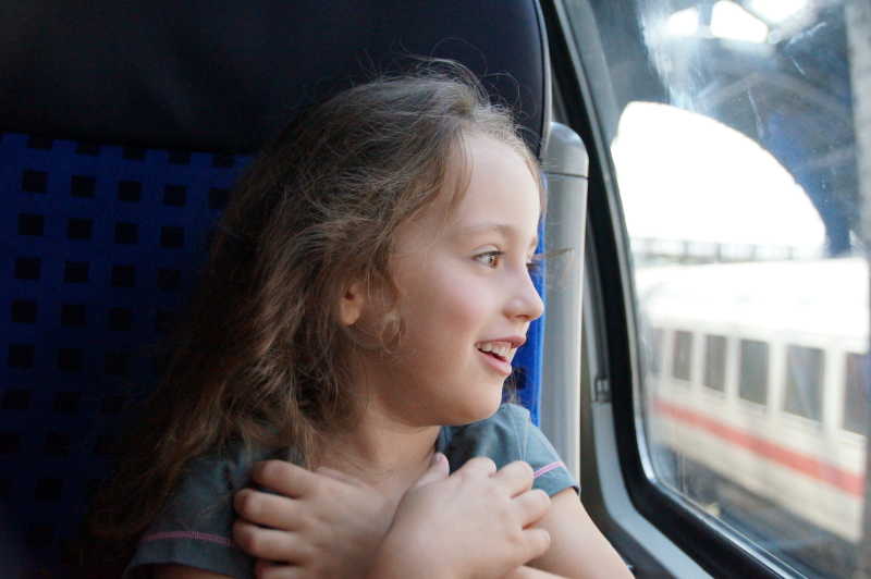 Ein kleines Mädchen schaut staunend aus dem Fenster eines Zuges, der im Bahnhof steht.