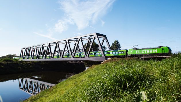 Ein grüner FlixTrain fährt über eine Eisenbrücke. 