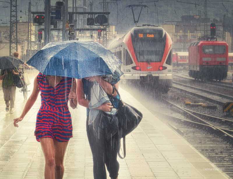 Zwei Frauen unter einem Regenschirm laufen in starkem Regen über den Bahnsteig