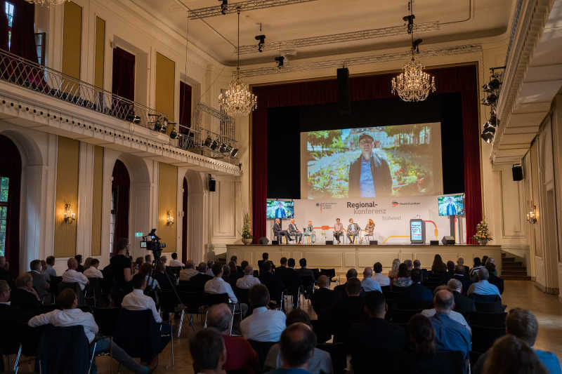 Blick in den Saal der Regionalkonferenz in Kurfürstlichen Schloss Mainz. Auf der Bühne sitzen Landespolitikerinnen und -politiker.