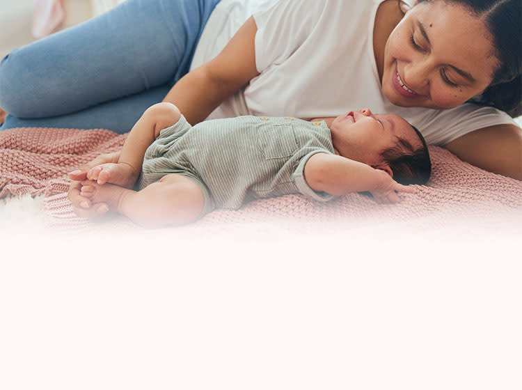 A mom playing with her baby laying down on a blanket