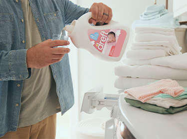Liquid detergent is poured into the washing machine to get poop stain out of baby clothes