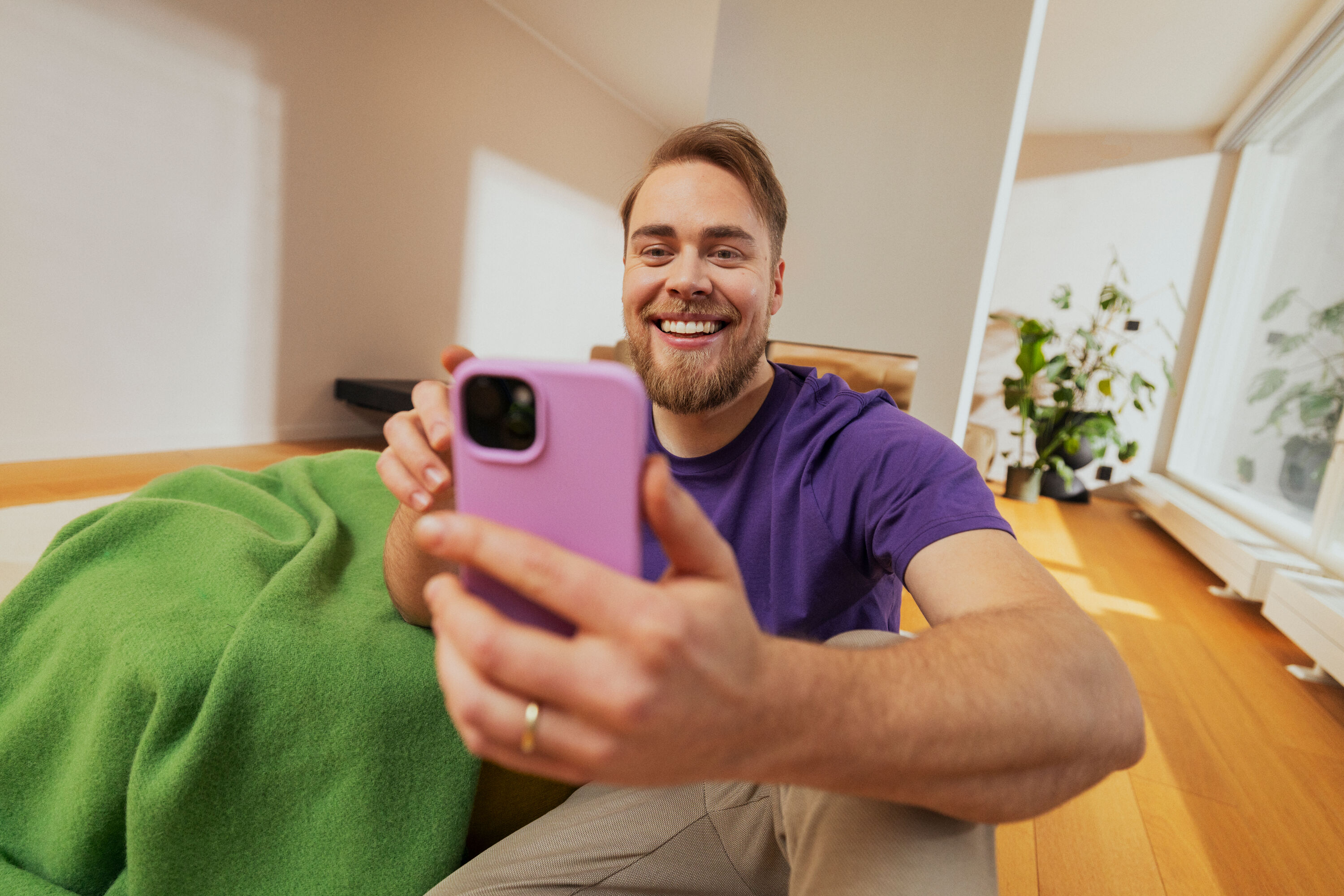 En man ler medan han använder sin telefon med rosa skal.