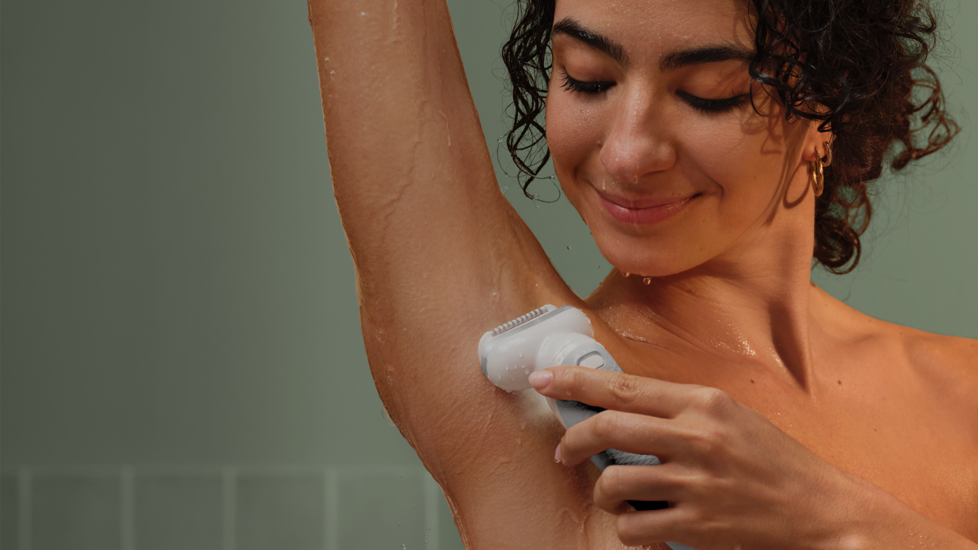 Žena koristi depilator ispod pazuha dok joj se voda sliva niz kožu.