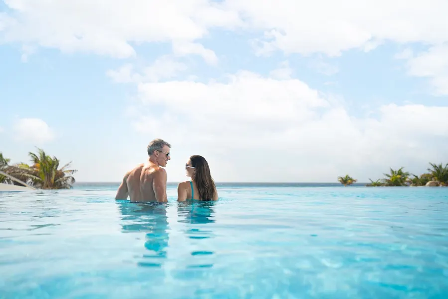 A couple enjoying a refreshing swim in a pool, surrounded by clear blue water and basking in the sunlight.