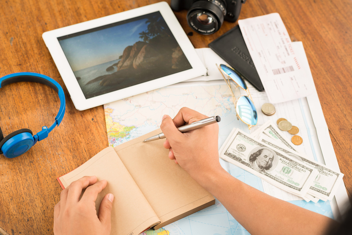 Hands of man planning his vacations, writing in a notebook