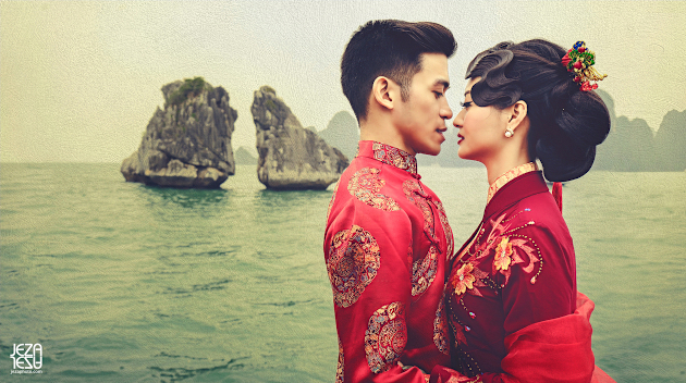 Bride and Groom in Vietnamese Áo dài, standing on a junk boat floating by a twin rock formation in Ha Long Bay, Vietnam