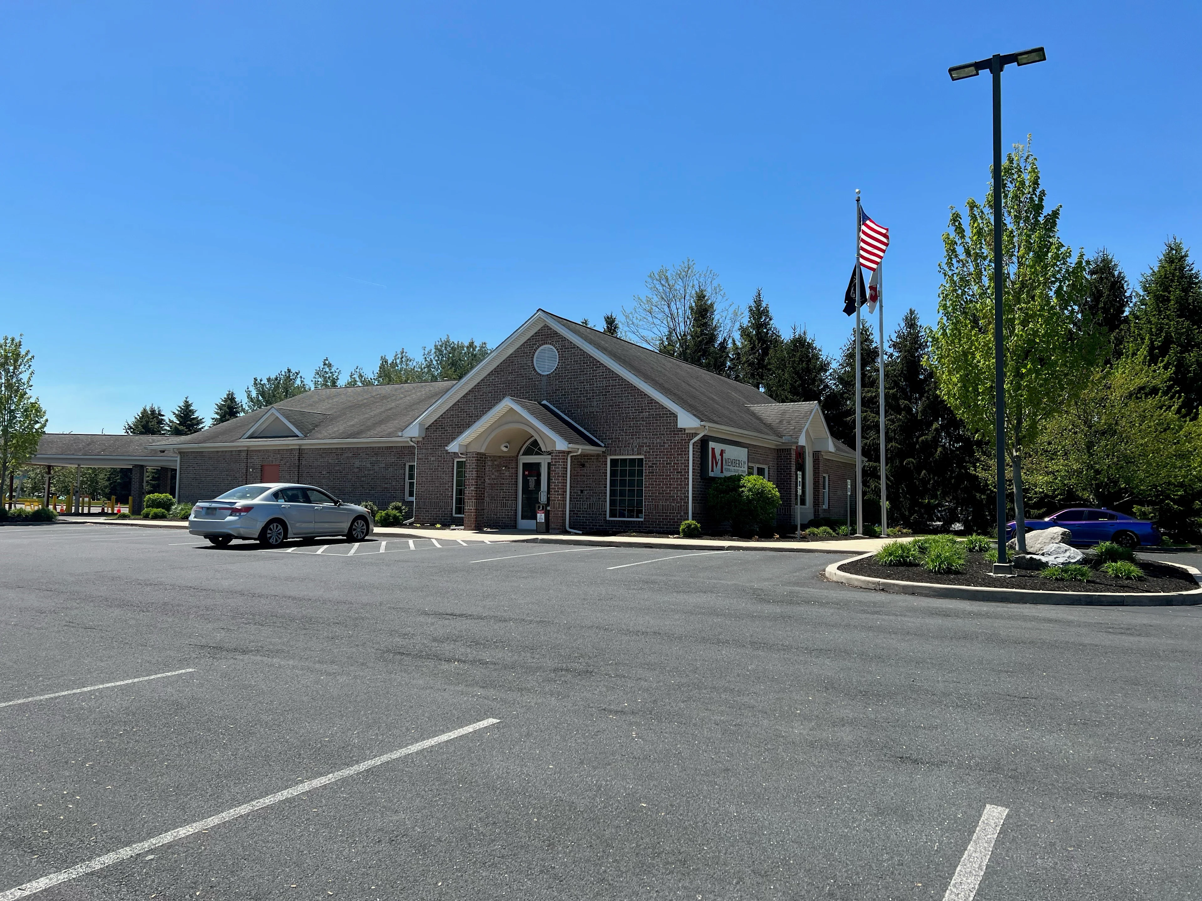 Walnut Bottom red brick Members 1st Federal Credit Union building with American flag, parking lot with cars, and landscaped entrance under clear blue sky.