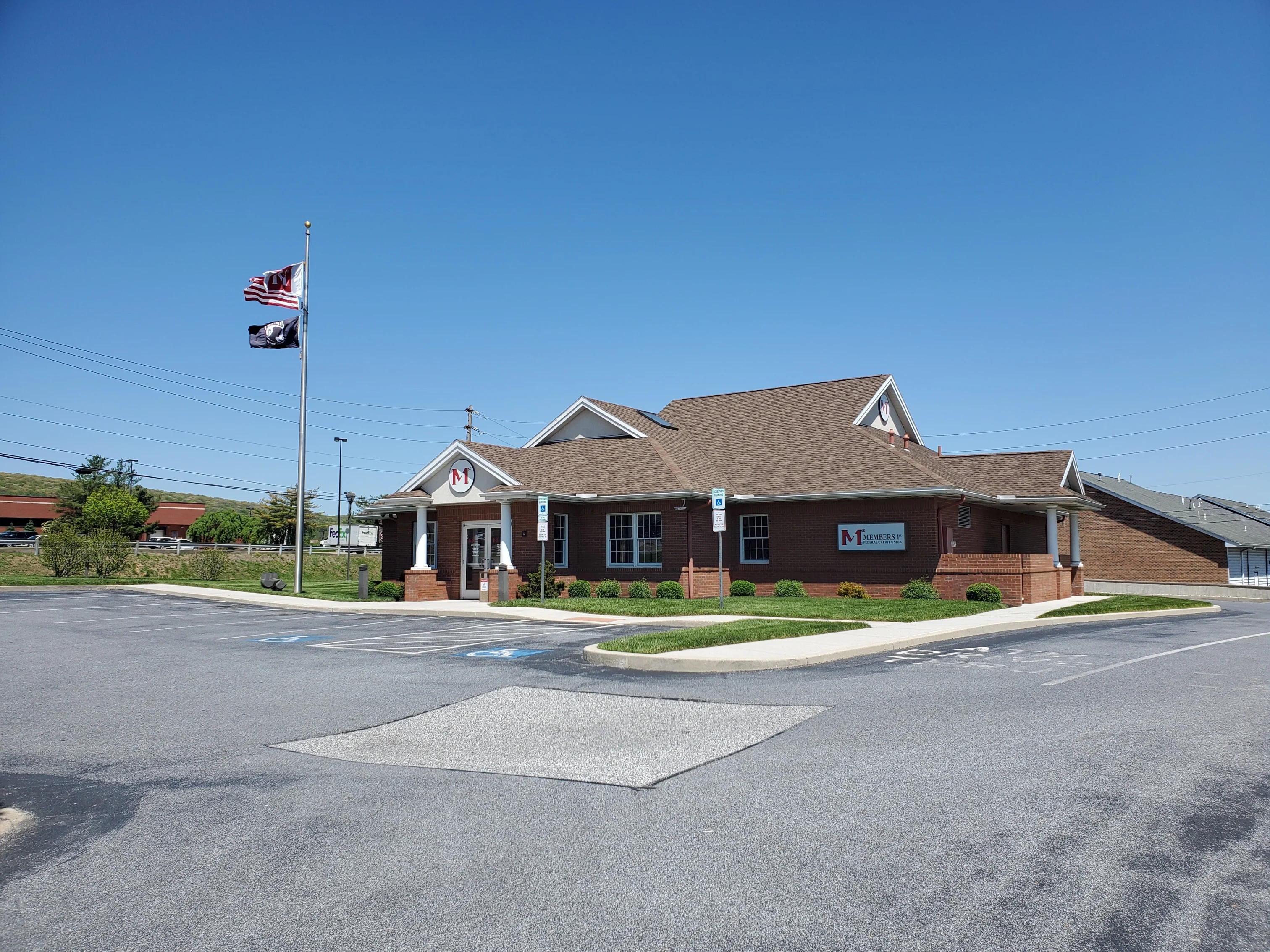 Whiteford Road Members 1st Federal Credit Union branch with white columns and American flag on pole under clear blue sky with parking lot in front.