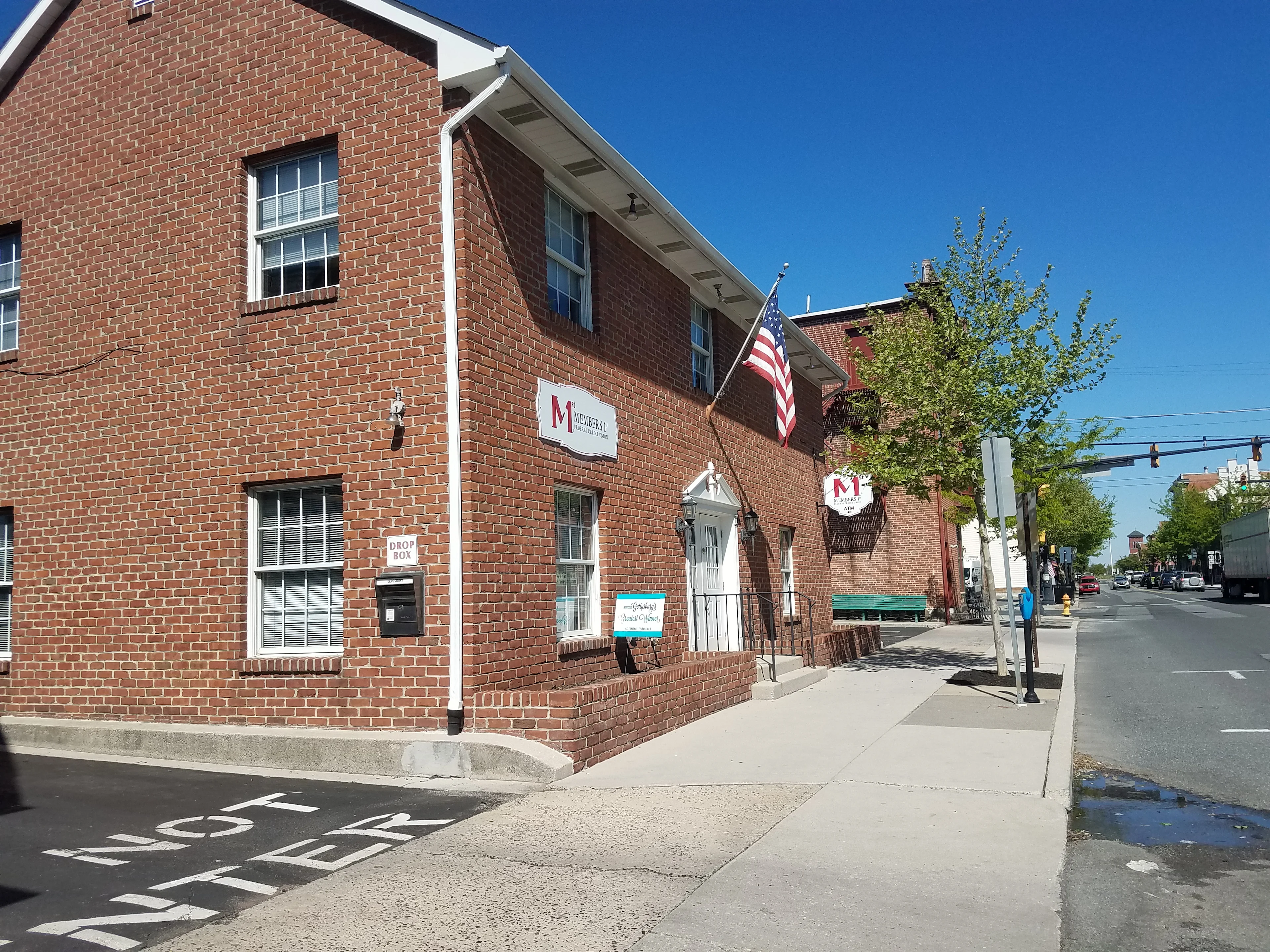 Red brick building with white-trimmed windows and American flag on street corner under clear blue sky.