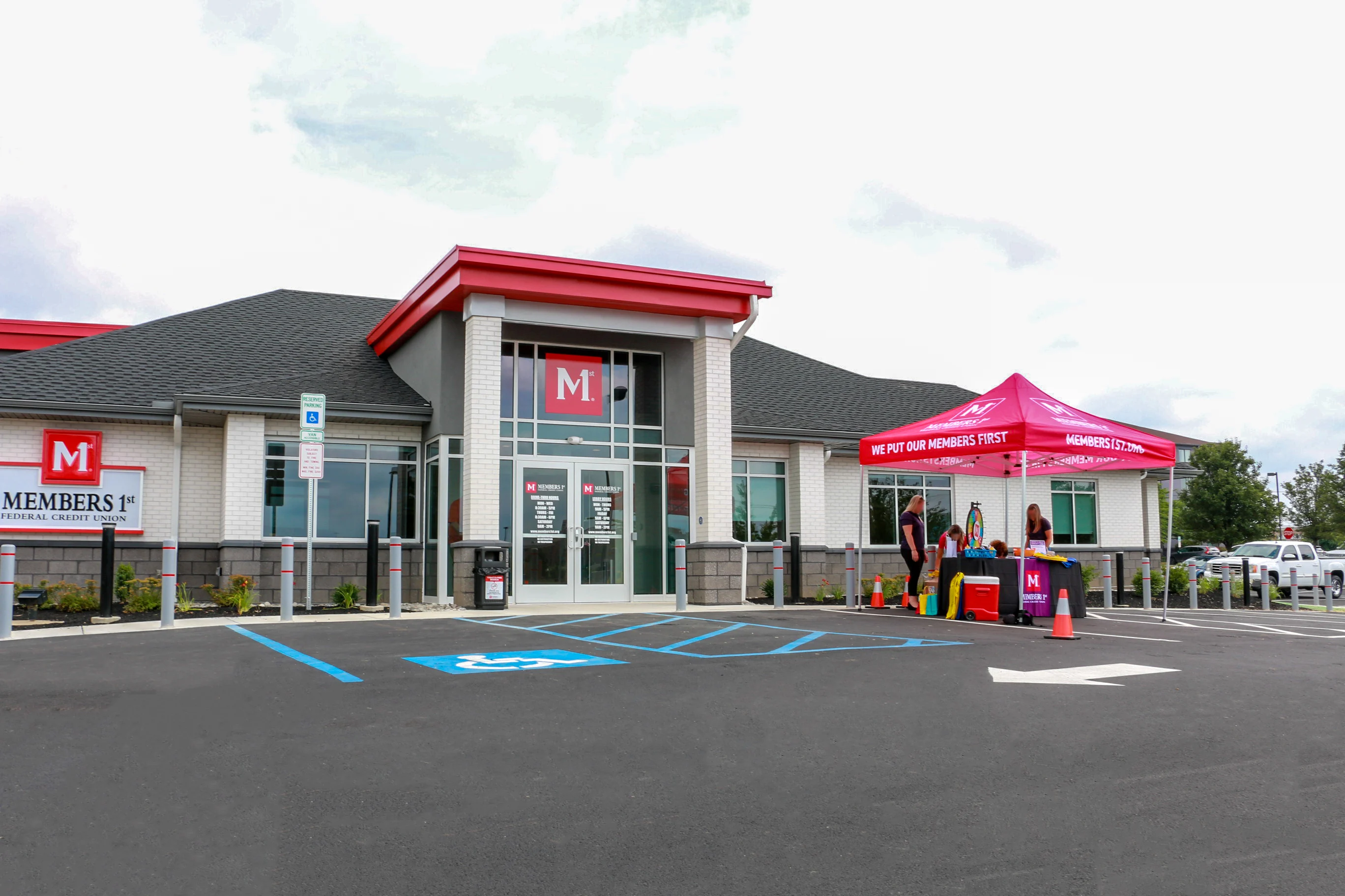 Emrick Boulevard Members 1st Federal Credit Union building with red roof and signage, accessible parking, and promotional tent outside.