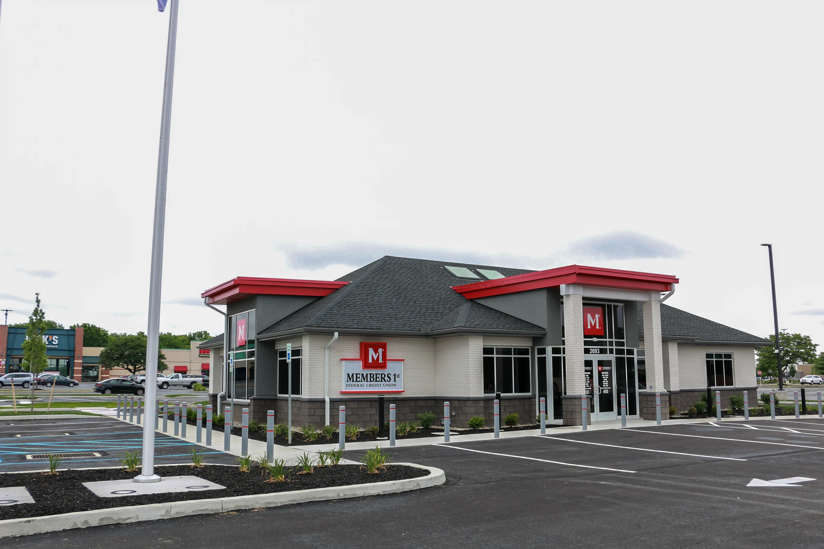 Whitehall Members 1st Federal Credit Union building with red accents, dark roof, and parking lot under cloudy sky.