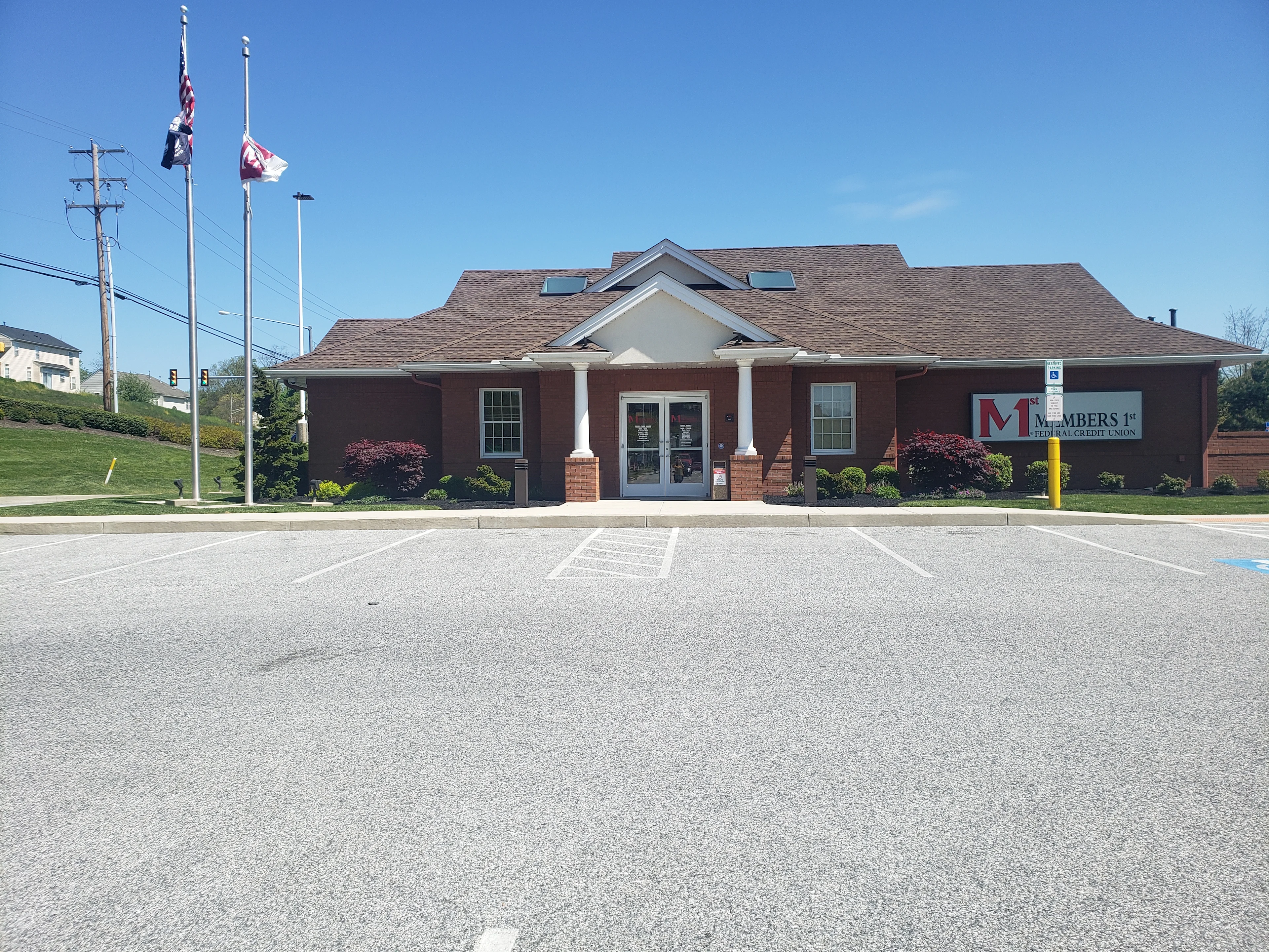 Red brick Members 1st Federal Credit Union building with white columns and flags under clear blue sky with parking lot.