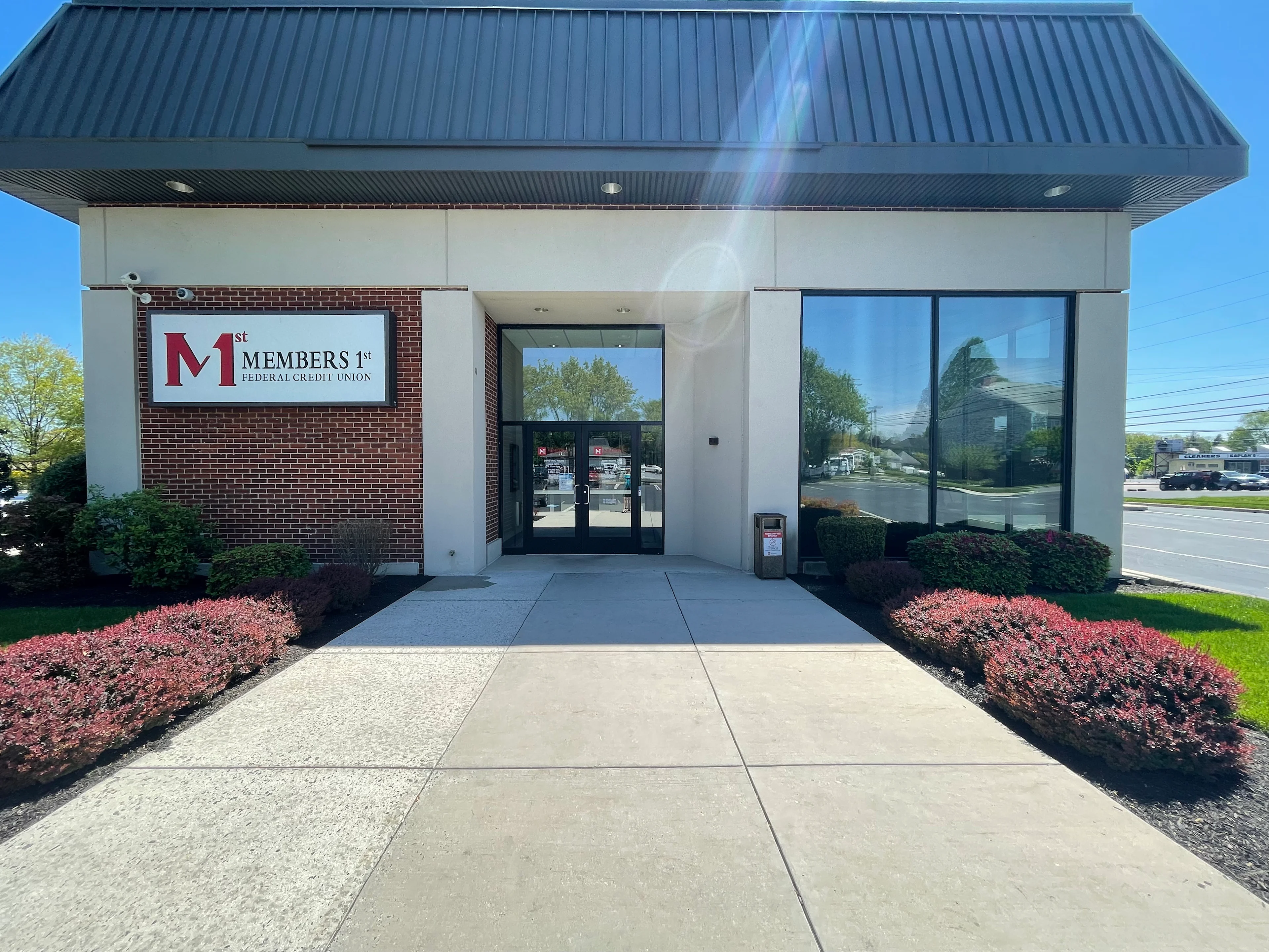 Camp Hill Members 1st Federal Credit Union branch exterior with brick facade, glass entrance, and landscaped pink shrubs.