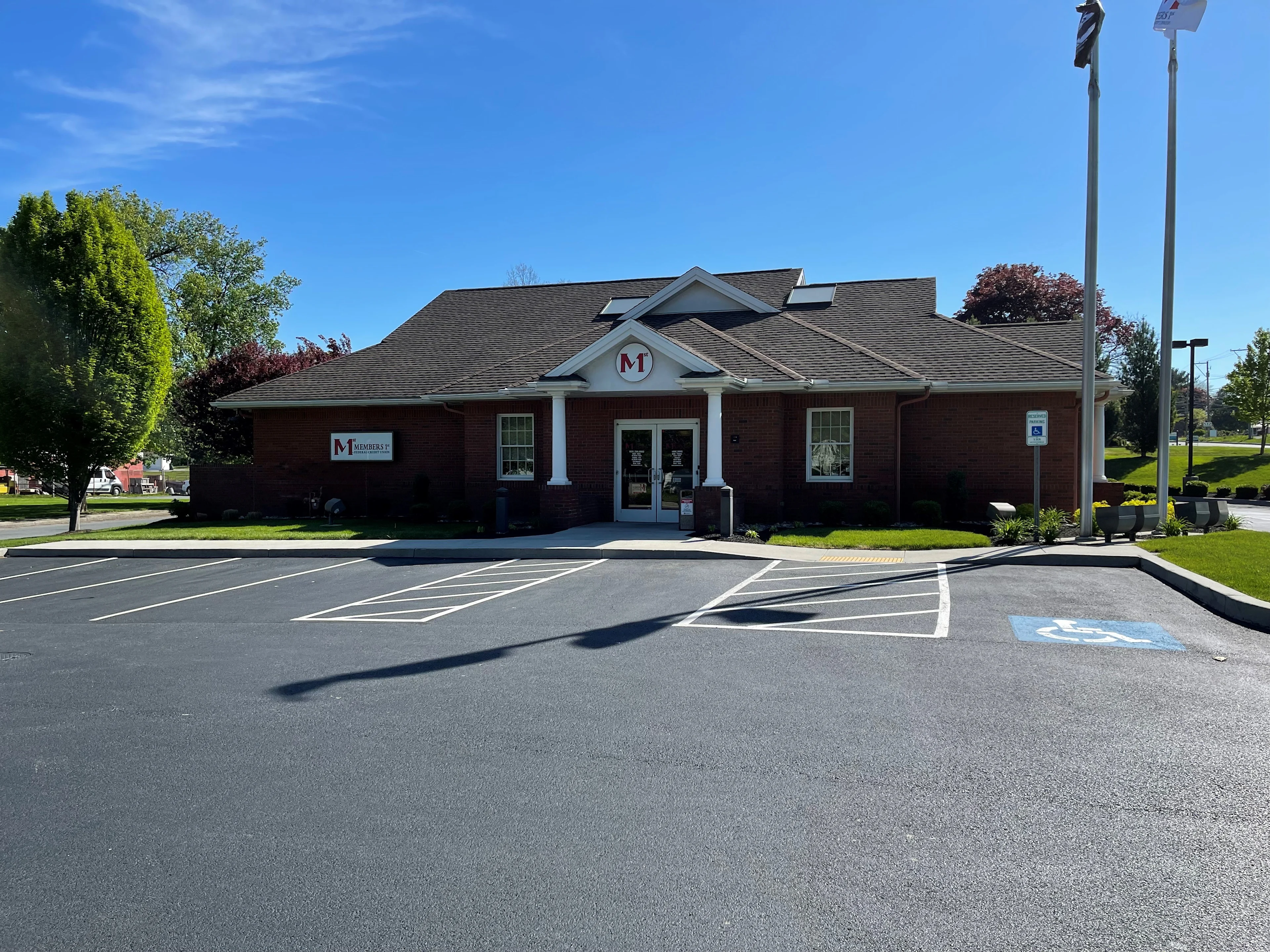 Hershey red brick Members 1st Federal Credit Union building with white columns and M logo, parking lot with handicap space, under clear blue sky.