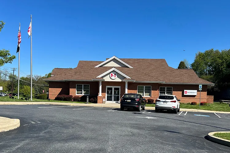 Colonial Park Members 1st Federal Credit Union branch with brown roof and white columns, two cars parked in front under clear blue sky.