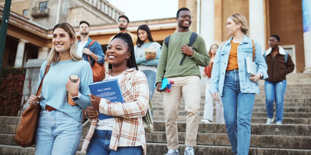 Diverse group of college students walking down outdoor campus stairs carrying books and backpacks in casual clothing.