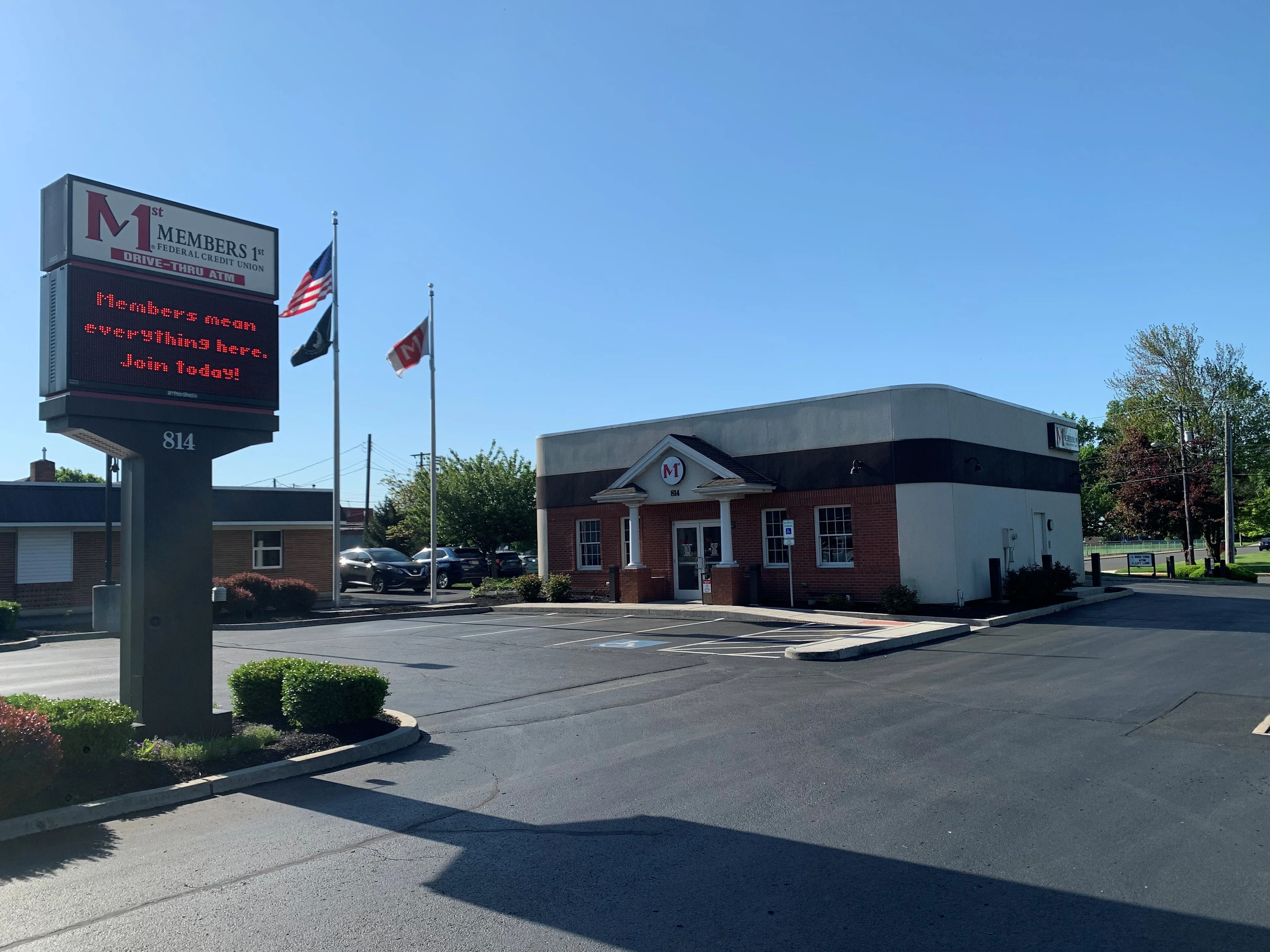 Members 1st Federal Credit Union building with digital sign and three flags in front under clear blue sky.