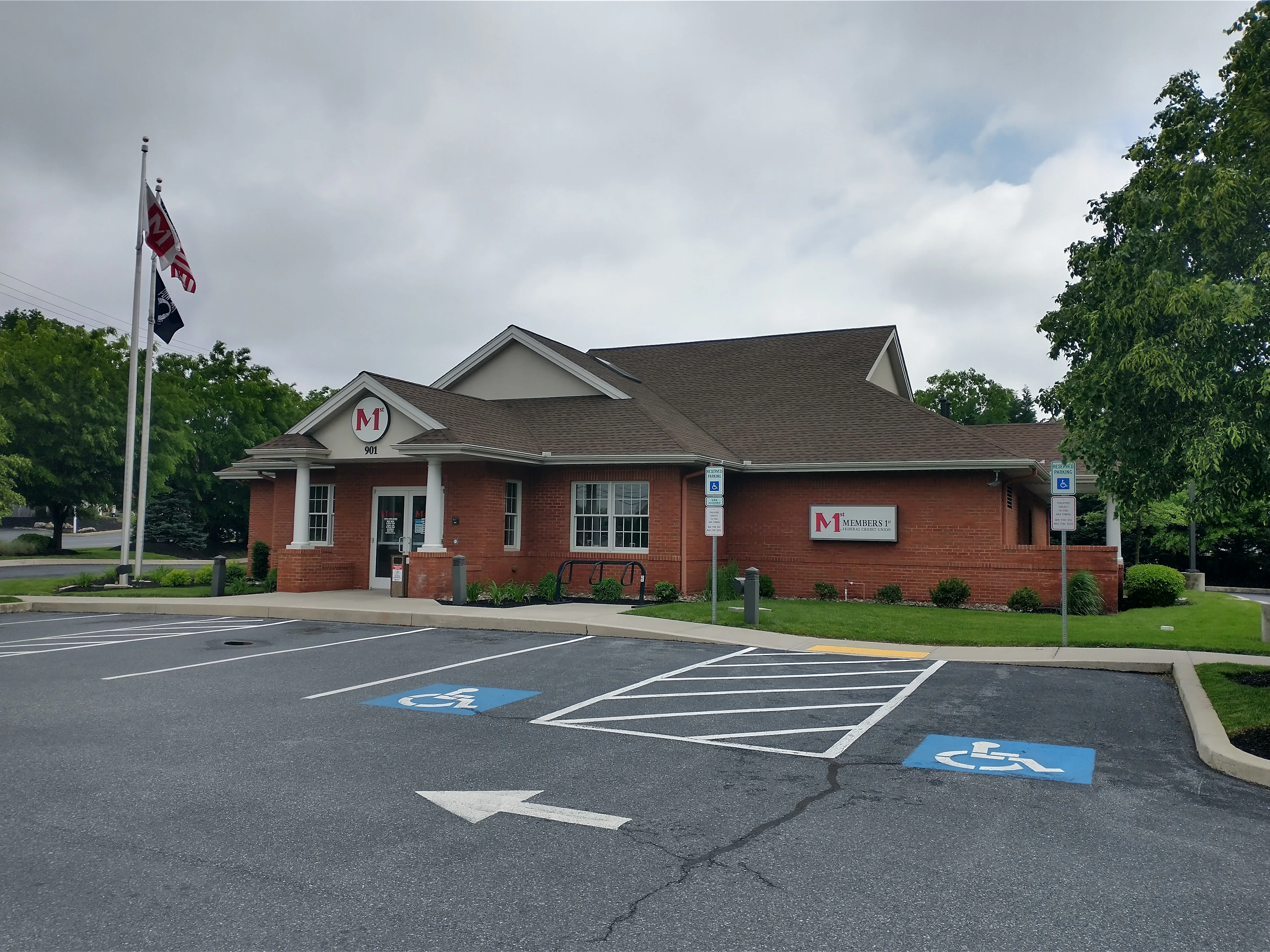 Lititz Pike red brick Members 1st Federal Credit Union building with white trim and dark roof, accessible parking spaces in front, under cloudy sky with trees.