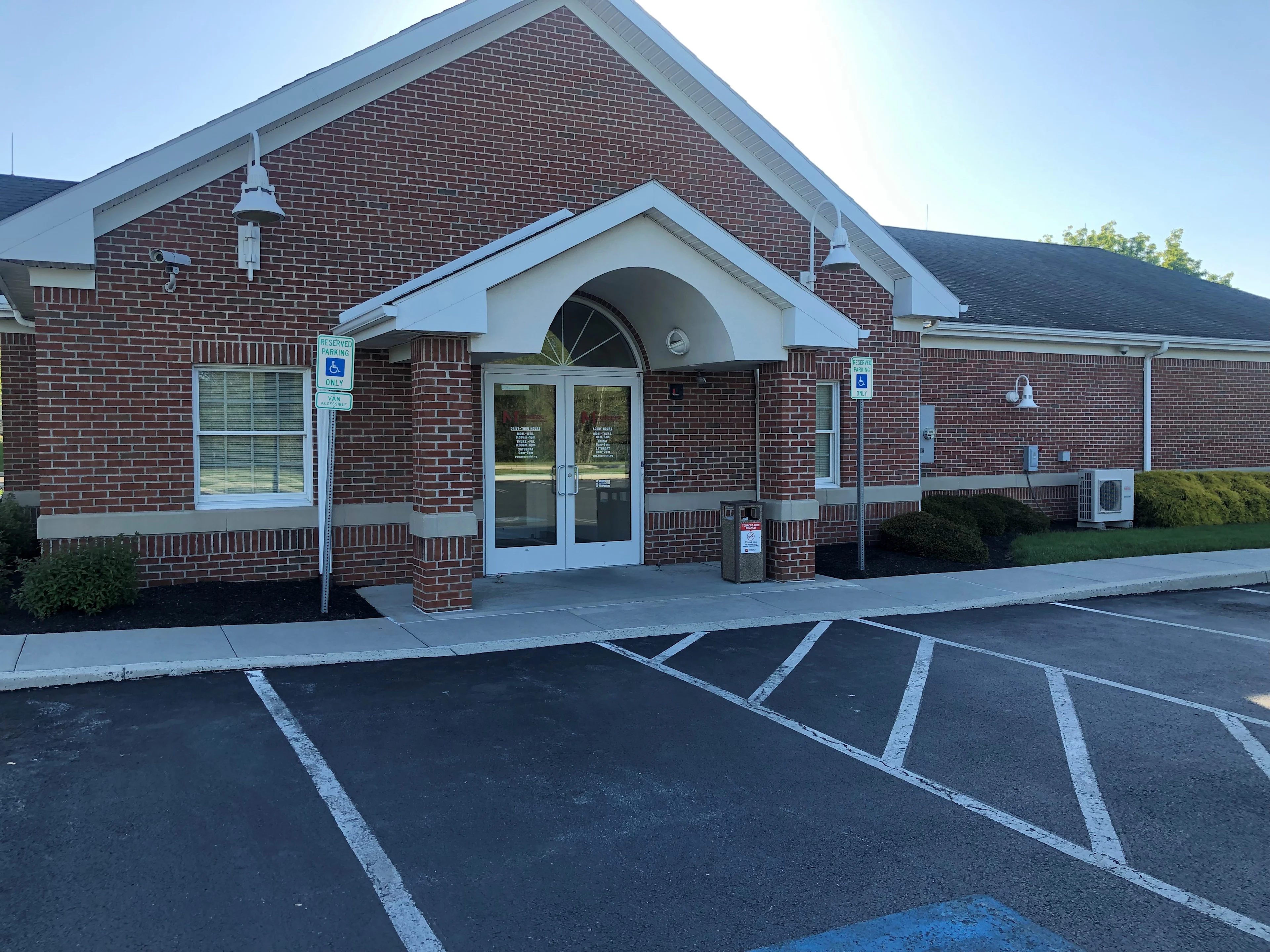Red brick building entrance with white arched portico, glass double doors, and accessible parking spaces in front.