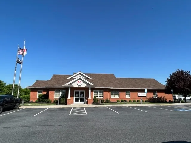 Greenfield red brick Members 1st Federal Credit Union building with white columns and brown roof under clear blue sky with American flag on flagpole in front.