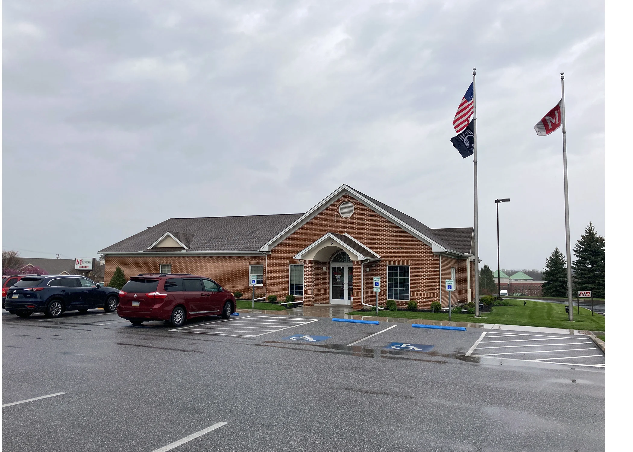 Red brick commercial building with American and POW flags flying in front, parking lot with accessible spaces visible.