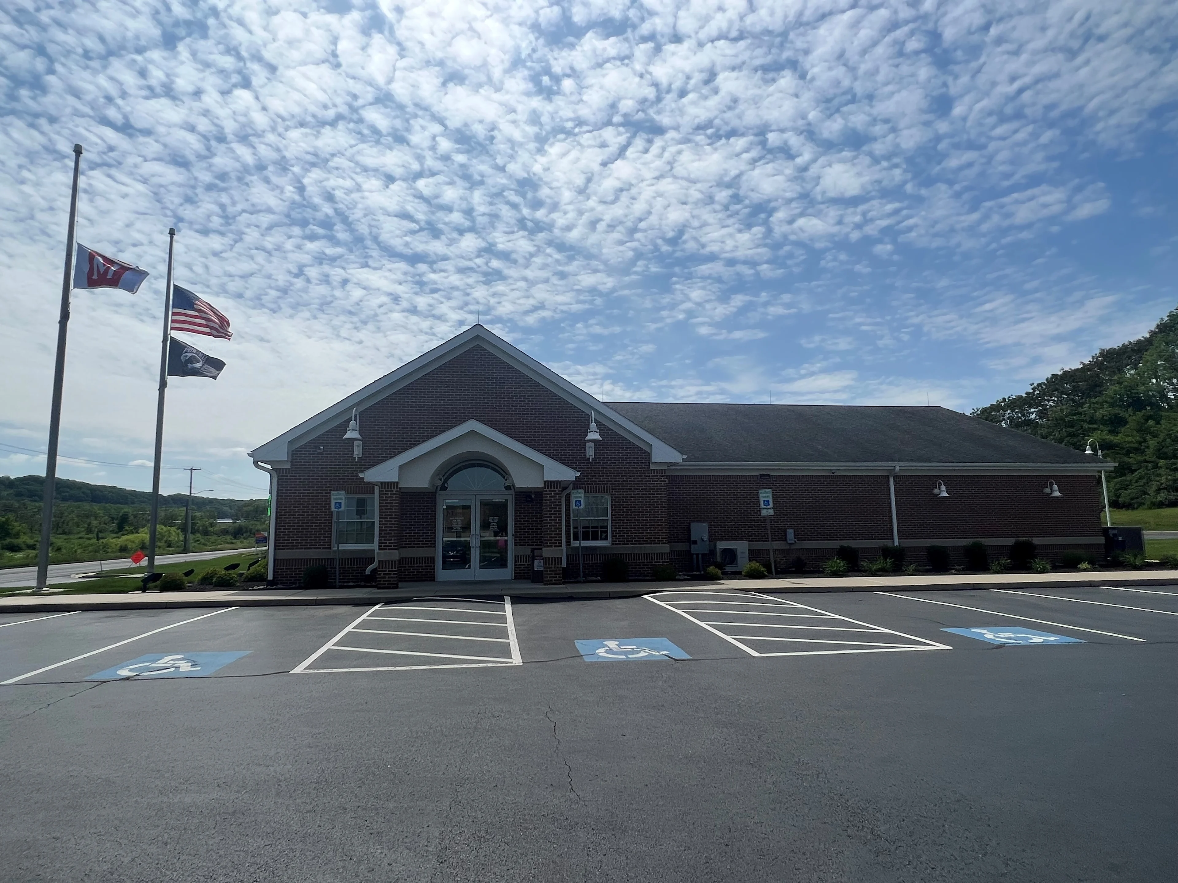 Red brick building with arched entrance and parking lot, three flags flying at half-mast under cloudy blue sky.