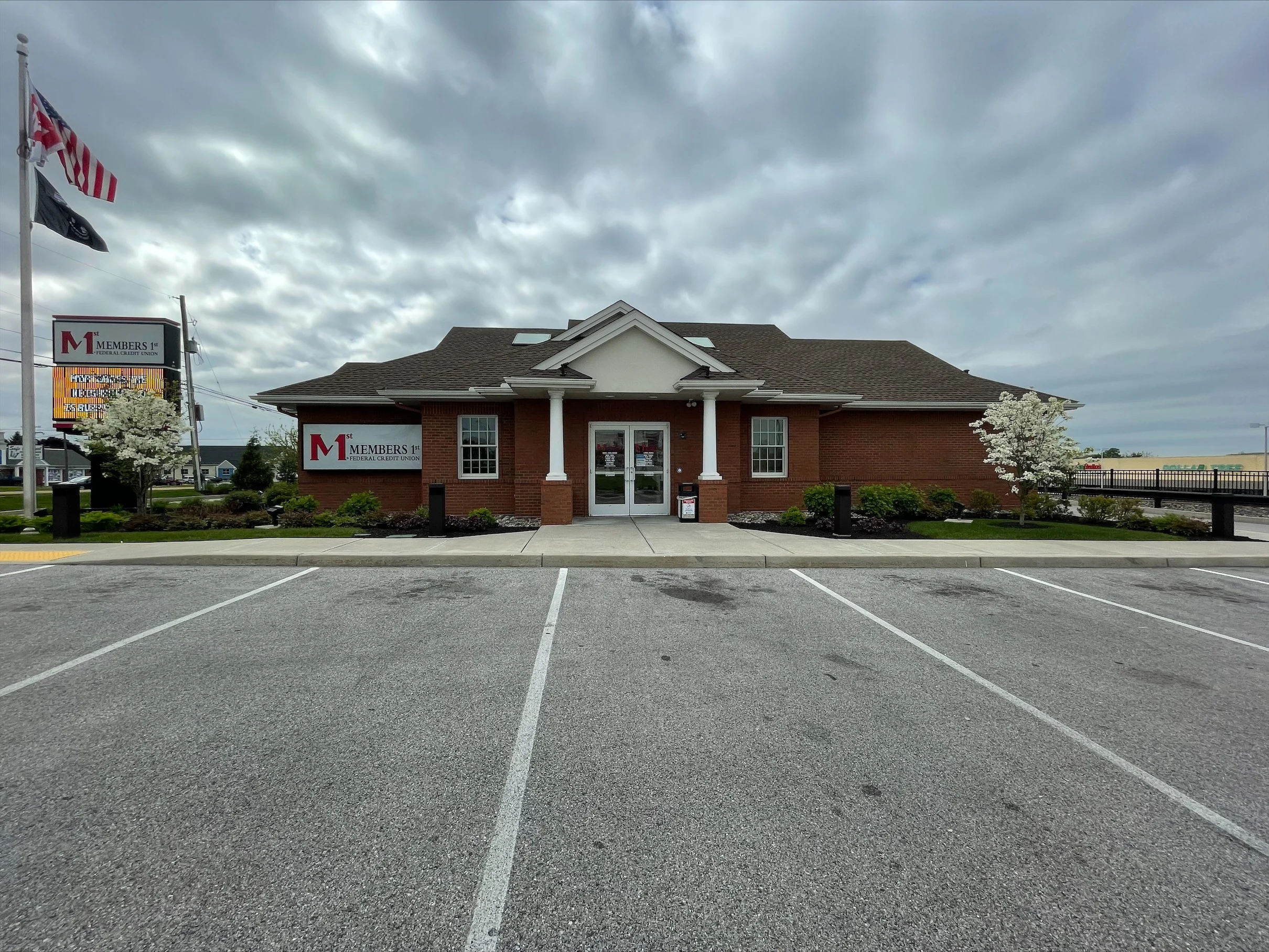 Red brick Members 1st Federal Credit Union building with white columns and glass entrance doors under cloudy sky.