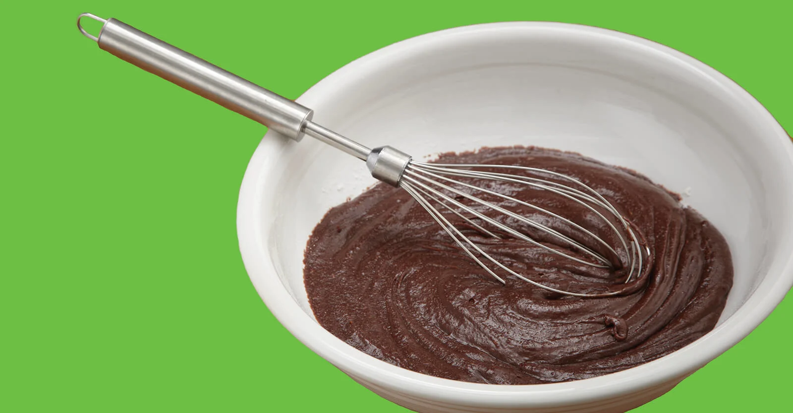 Metal whisk resting in white bowl filled with smooth chocolate batter on green background.