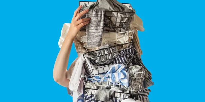 Person holding overflowing wire laundry basket filled with clothes against bright blue background